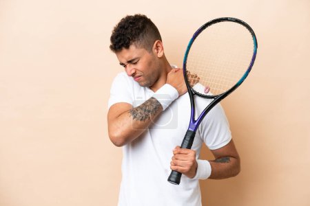 Téléchargez les photos : Jeune homme beau brésilien jouant au tennis isolé sur fond beige souffrant de douleur à l'épaule pour avoir fait un effort - en image libre de droit