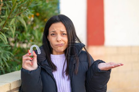 Photo for Young woman holding invisible braces at outdoors making doubts gesture while lifting the shoulders - Royalty Free Image