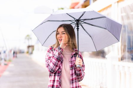 Junge hübsche Rumänin hält draußen einen Regenschirm und flüstert etwas