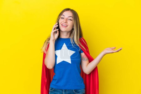 Super Hero Romanian woman isolated on yellow background keeping a conversation with the mobile phone with someone