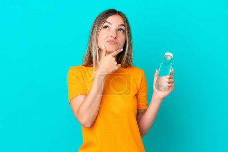 Photo for Young Romanian woman with a bottle of water isolated on blue background having doubts - Royalty Free Image