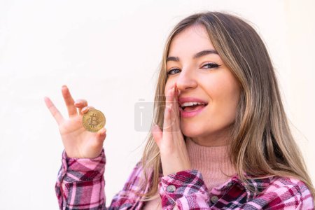 Young pretty Romanian woman holding a Bitcoin at outdoors whispering something