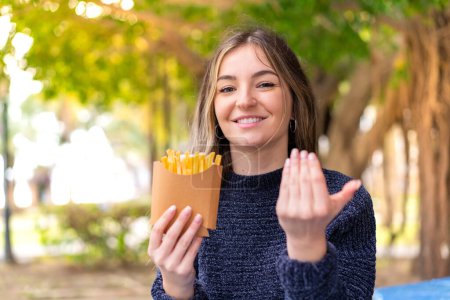 Photo for Young pretty Romanian woman holding fried chips at outdoors inviting to come with hand. Happy that you came - Royalty Free Image