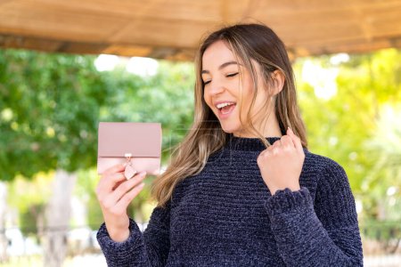 Photo for Young pretty Romanian woman holding a wallet at outdoors celebrating a victory - Royalty Free Image
