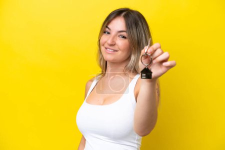 Téléchargez les photos : Jeune femme roumaine tenant les clés de la maison isolées sur fond jaune avec une expression heureuse - en image libre de droit
