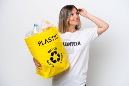 Téléchargez les photos : Jeune femme roumaine tenant un sac de recyclage plein de plastique à recycler isolé sur fond blanc ayant des doutes et avec une expression du visage confuse - en image libre de droit