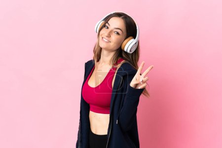 Photo for Young Romanian sport woman isolated on pink background smiling and showing victory sign - Royalty Free Image