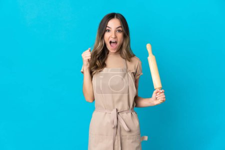 Photo for Young Romanian woman holding a rolling pin isolated on blue background celebrating a victory in winner position - Royalty Free Image