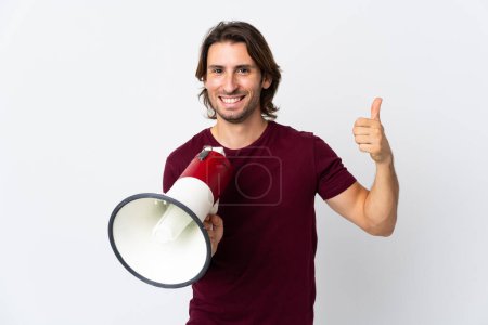 Photo for Young handsome man isolated on white background holding a megaphone with thumb up - Royalty Free Image