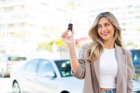 Téléchargez les photos : Jolie femme uruguayenne blonde tenant des clés de voiture à l'extérieur avec une expression heureuse - en image libre de droit