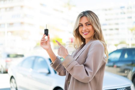 Téléchargez les photos : Jolie femme uruguayenne blonde tenant des clés de voiture à l'extérieur et le pointant - en image libre de droit