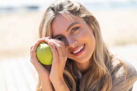 Téléchargez les photos : Jeune jolie blonde uruguayenne en plein air tenant une pomme - en image libre de droit