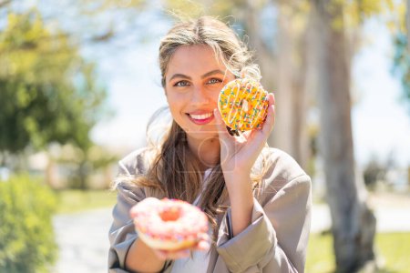Foto de Joven guapa rubia uruguaya al aire libre sosteniendo rosquillas con expresión feliz - Imagen libre de derechos