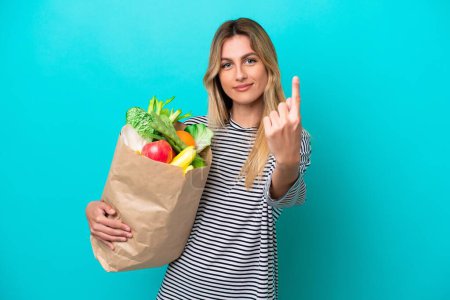 Photo for Young Uruguayan woman holding a grocery shopping bag isolated on blue background doing coming gesture - Royalty Free Image
