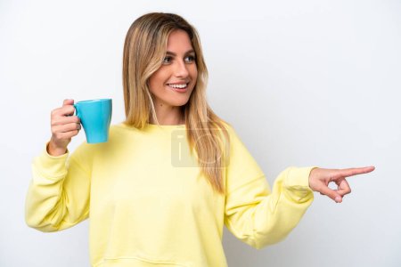 Téléchargez les photos : Jeune femme uruguayenne tenant une tasse de café isolée sur fond blanc pointant vers le côté pour présenter un produit - en image libre de droit