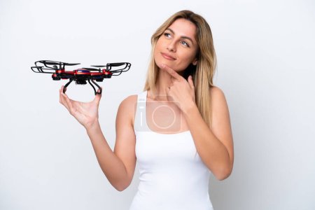Téléchargez les photos : Jeune femme uruguayenne tenant un drone isolé sur fond blanc ayant des doutes tout en levant les yeux - en image libre de droit