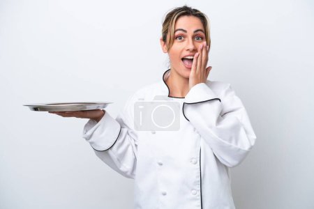 Foto de Joven chef mujer con bandeja aislada sobre fondo blanco con expresión facial sorpresa y conmocionada - Imagen libre de derechos