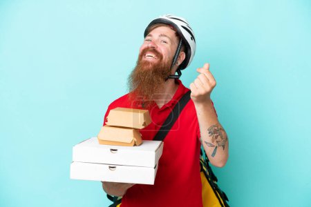 Téléchargez les photos : Livreur tenant des pizzas et des hamburgers isolés sur fond bleu faisant geste d'argent - en image libre de droit