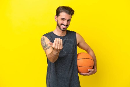 Téléchargez les photos : Beau jeune joueur de basket isolé sur fond jaune invitant à venir avec la main. Heureux que tu sois venu - en image libre de droit