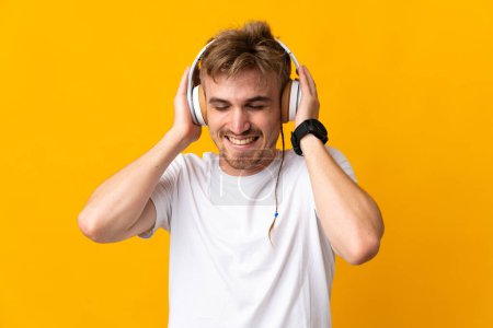 Téléchargez les photos : Jeune homme blond beau isolé sur fond jaune écoutant de la musique - en image libre de droit