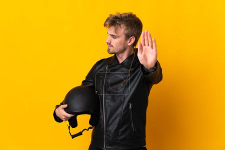 Foto de Hombre con un casco de motocicleta aislado sobre fondo amarillo haciendo gesto de parada y decepcionado - Imagen libre de derechos
