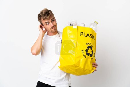 Foto de Joven hombre rubio sosteniendo una bolsa de reciclaje llena de papel para reciclar aislado sobre fondo blanco pensando en una idea - Imagen libre de derechos