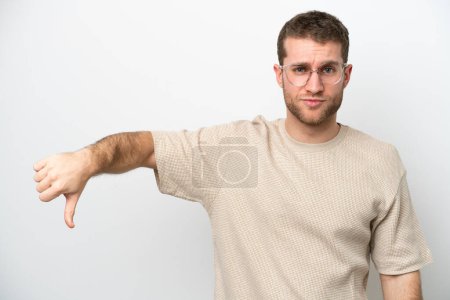 Foto de Joven hombre caucásico aislado sobre fondo blanco mostrando el pulgar hacia abajo con expresión negativa - Imagen libre de derechos