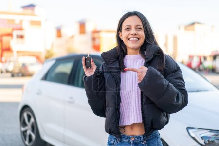 Foto de Mujer joven al aire libre sosteniendo las llaves del coche al aire libre y señalándolo - Imagen libre de derechos
