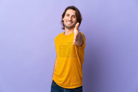 Photo for Young handsome man isolated on purple background shaking hands for closing a good deal - Royalty Free Image