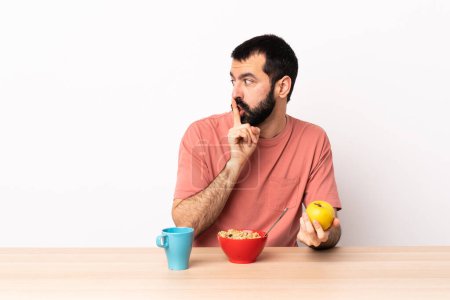 Téléchargez les photos : Homme caucasien prendre le petit déjeuner dans une table montrant un signe de silence geste mettre le doigt dans la bouche. - en image libre de droit