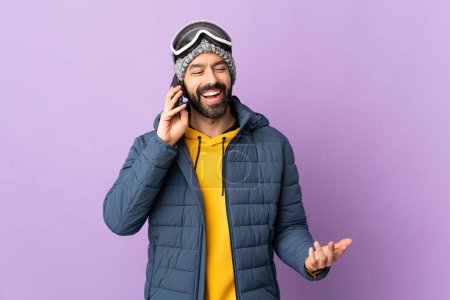 Téléchargez les photos : Skier homme avec des lunettes de snowboard sur fond violet isolé garder une conversation avec le téléphone portable avec quelqu'un - en image libre de droit