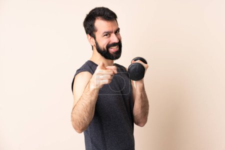 Téléchargez les photos : Homme de sport caucasien avec barbe faisant haltérophilie sur fond isolé pointant devant avec expression heureuse - en image libre de droit