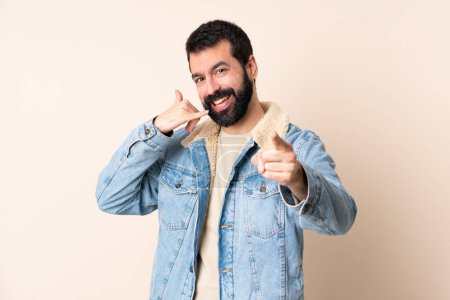 Téléchargez les photos : Homme caucasien avec barbe sur fond isolé faisant geste de téléphone et pointant devant - en image libre de droit