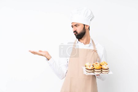 Photo for Young man holding muffin cake over isolated white background holding copyspace with doubts - Royalty Free Image