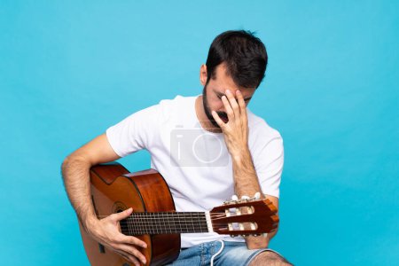 Photo for Young man with guitar over isolated blue background with tired and sick expression - Royalty Free Image