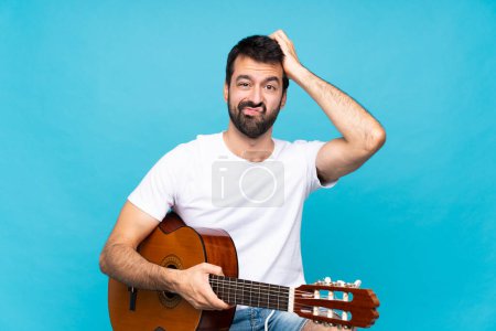 Téléchargez les photos : Jeune homme avec guitare sur fond bleu isolé avec une expression de frustration et de ne pas comprendre - en image libre de droit
