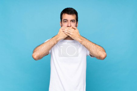 Téléchargez les photos : Jeune homme avec barbe sur fond bleu isolé couvrant la bouche avec les mains - en image libre de droit