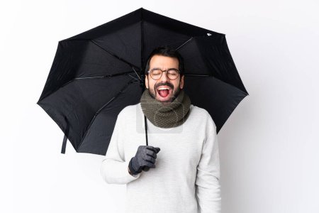 Photo for Caucasian handsome man with beard holding an umbrella over isolated white wall shouting to the front with mouth wide open - Royalty Free Image