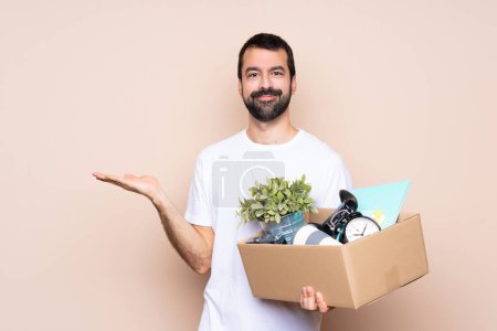Photo for Man holding a box and moving in new home over isolated background holding copyspace imaginary on the palm to insert an ad - Royalty Free Image