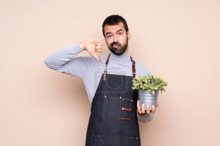 Téléchargez les photos : Homme tenant une plante sur fond isolé montrant pouce vers le bas - en image libre de droit