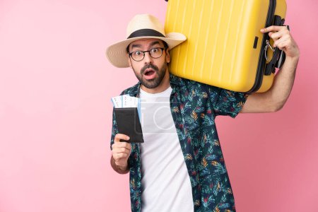 Foto de Joven hombre caucásico sobre fondo aislado en vacaciones con maleta y pasaporte y sorprendido - Imagen libre de derechos
