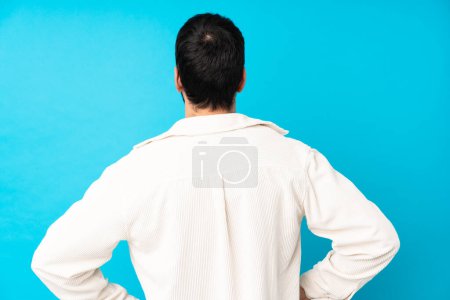 Foto de Joven hombre guapo con chaqueta de pana blanca sobre fondo azul aislado en la posición posterior - Imagen libre de derechos