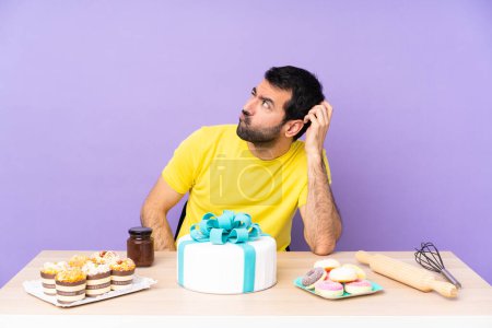 Foto de Hombre en una mesa con un pastel grande teniendo dudas mientras se rasca la cabeza - Imagen libre de derechos