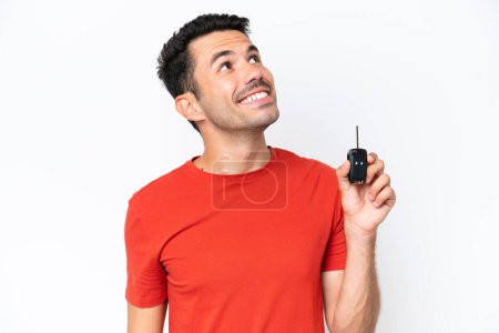 Foto de Joven hombre guapo sosteniendo las llaves del coche sobre fondo blanco aislado mirando hacia arriba mientras sonríe - Imagen libre de derechos