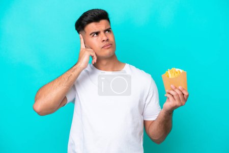 Photo for Young caucasian man catching french fries isolated on blue background having doubts and thinking - Royalty Free Image