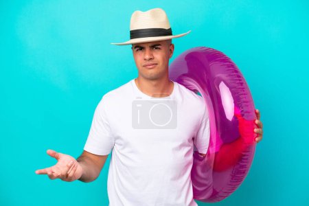 Photo for Young caucasian man holding air mattress isolated on blue background making doubts gesture while lifting the shoulders - Royalty Free Image