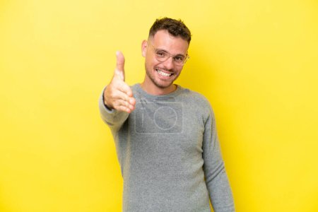 Photo for Young caucasian handsome man isolated on yellow background shaking hands for closing a good deal - Royalty Free Image