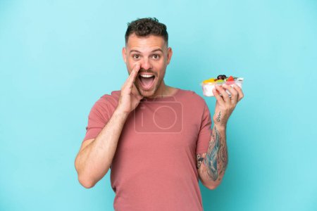 Photo for Young caucasian man holding a bowl of fruit isolated on blue background with surprise and shocked facial expression - Royalty Free Image