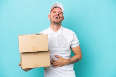 Photo for Delivery caucasian man isolated on blue background smiling a lot - Royalty Free Image