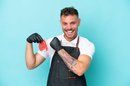 Photo for Butcher caucasian man wearing an apron and serving fresh cut meat isolated on blue background celebrating a victory - Royalty Free Image